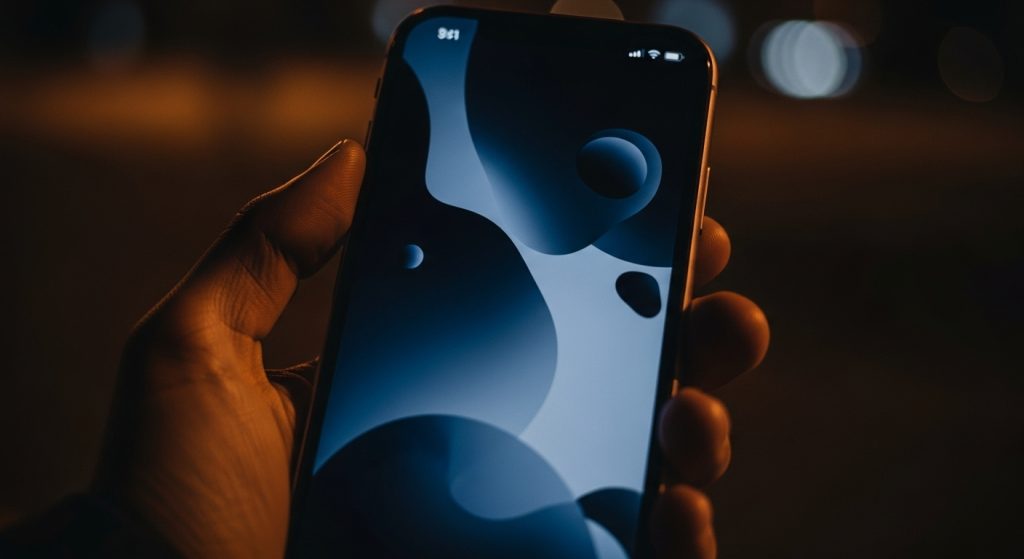 Aesthetic Wallpaper Backgrounds for iPhone HD & Minimal Styles 5 Close-up of an iPhone held in hand at night, screen glowing with dark navy blue and black aesthetic wallpaper