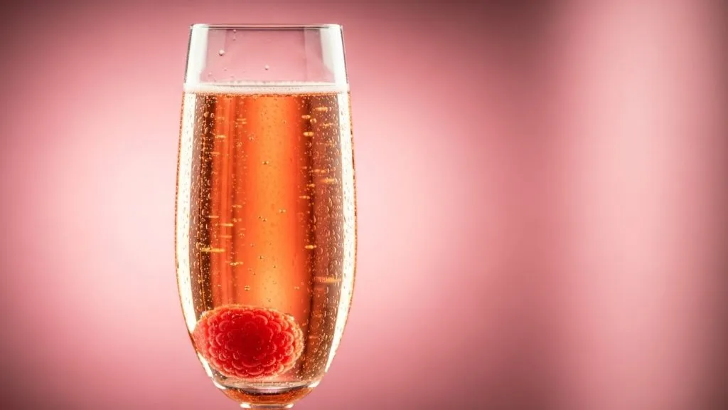15 Easy Tea Party Recipes Perfect for Bridal Showers 10 Champagne flute of peach bellini mocktail, raspberry slowly floating, soft condensation on glass, pink background