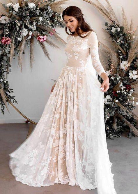 A stunning feature picture of a woman wearing an elegant ivory lace gown with long sheer sleeves and delicate floral embroidery. The flowing dress creates a soft romantic look while the floral arch background adds timeless wedding beauty and luxury fashion inspiration.