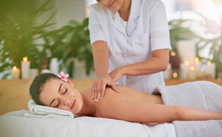 Relaxation massage therapy session featuring a woman receiving a calming spa back massage in a peaceful wellness setting with candles, soft towels, and a soothing self-care atmosphere.