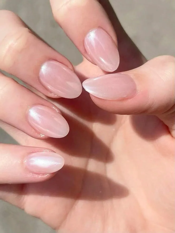 Soft pink almond-shaped nails with a glossy, pearlescent finish, featuring a clean, natural manicure look under warm sunlight.