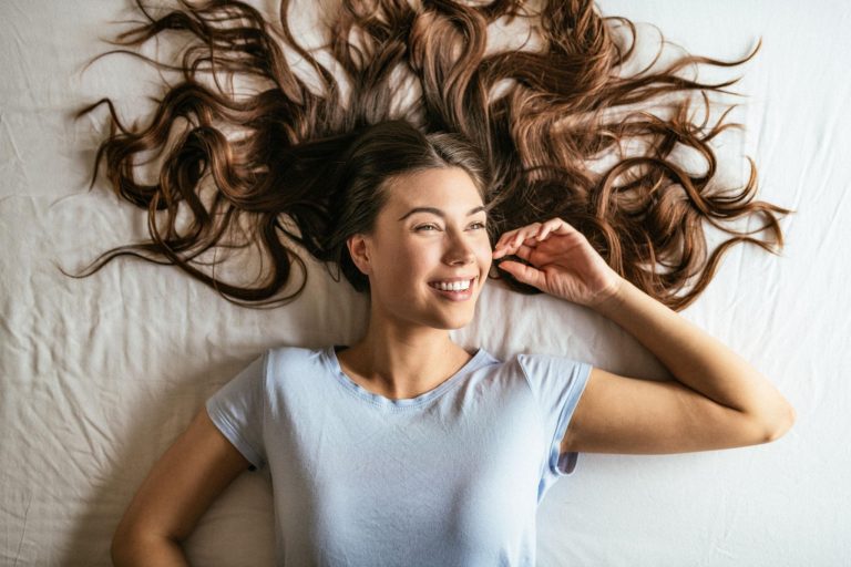 A beautiful beauty portrait featuring a woman with long healthy shiny hair surrounded by soft natural lighting and elegant typography promoting natural hair growth tips at home for stronger thicker and healthier hair.