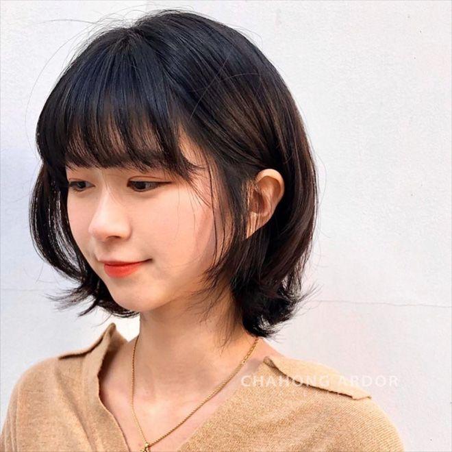 Woman with short layered bob haircut and soft bangs styled for a round face, featuring textured ends and volume that create a modern, flattering, and youthful hairstyle look for fine hair women