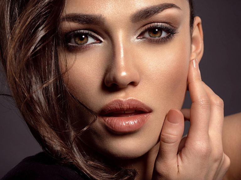 Close-up portrait of a woman with hazel-brown eyes wearing soft bronze eyeshadow, natural eyeliner, glowing skin, and nude lipstick, showcasing elegant makeup for hazel and brown eyes.
