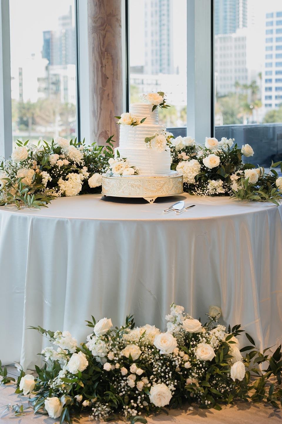 Elegant white wedding cake decorated with fresh roses on a luxury wedding dessert table.