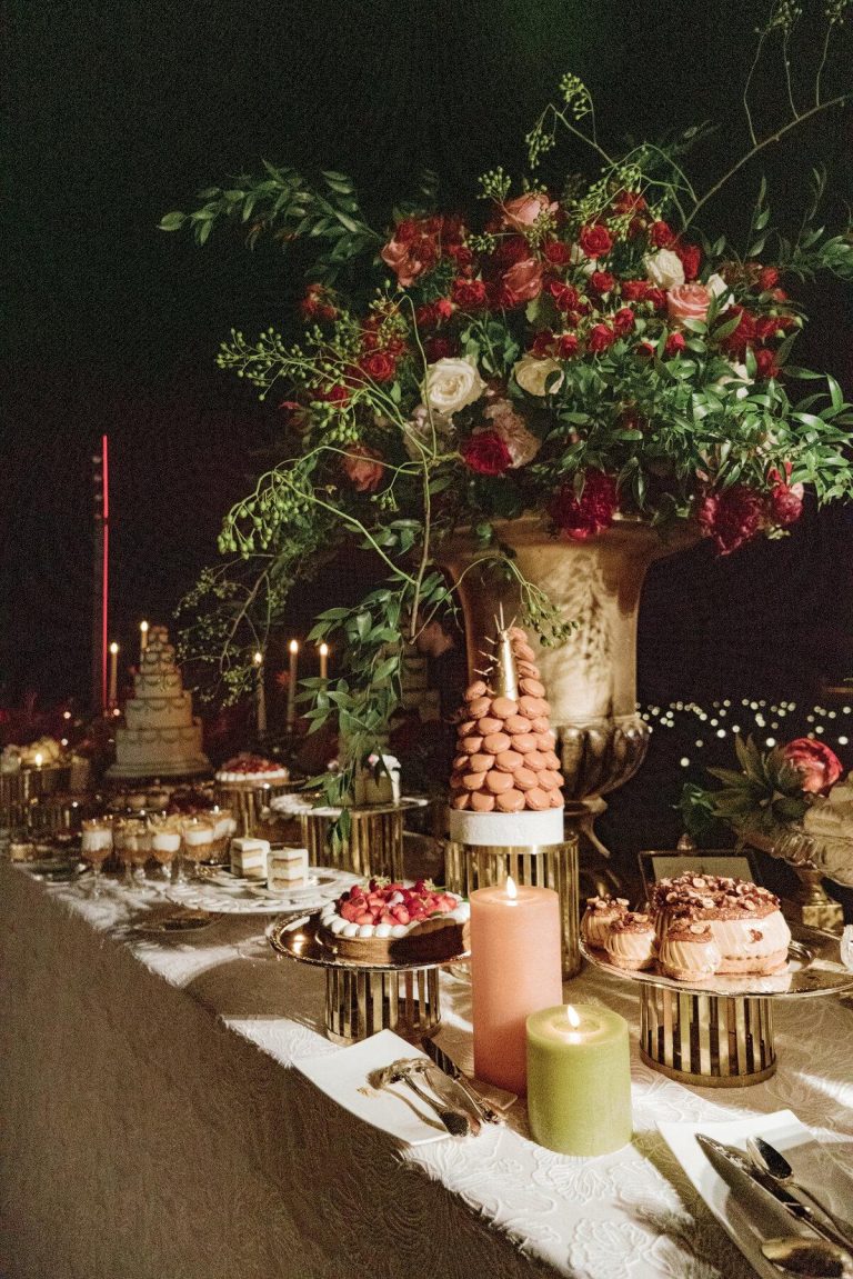 Elegant party dessert table featuring a celebration cake, cupcakes, macarons, and floral decorations.