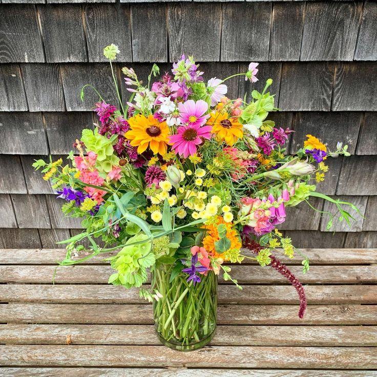 A rustic wooden table featuring colorful wildflowers in a vintage ceramic vase, soft natural sunlight, cottage garden background, professional floral photography.