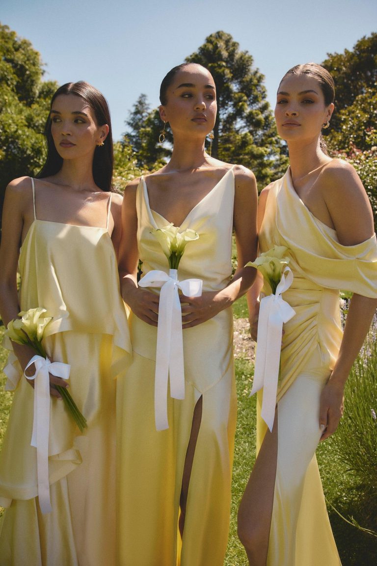 Bridesmaids wearing elegant butter yellow dresses standing together at a romantic outdoor wedding ceremony.