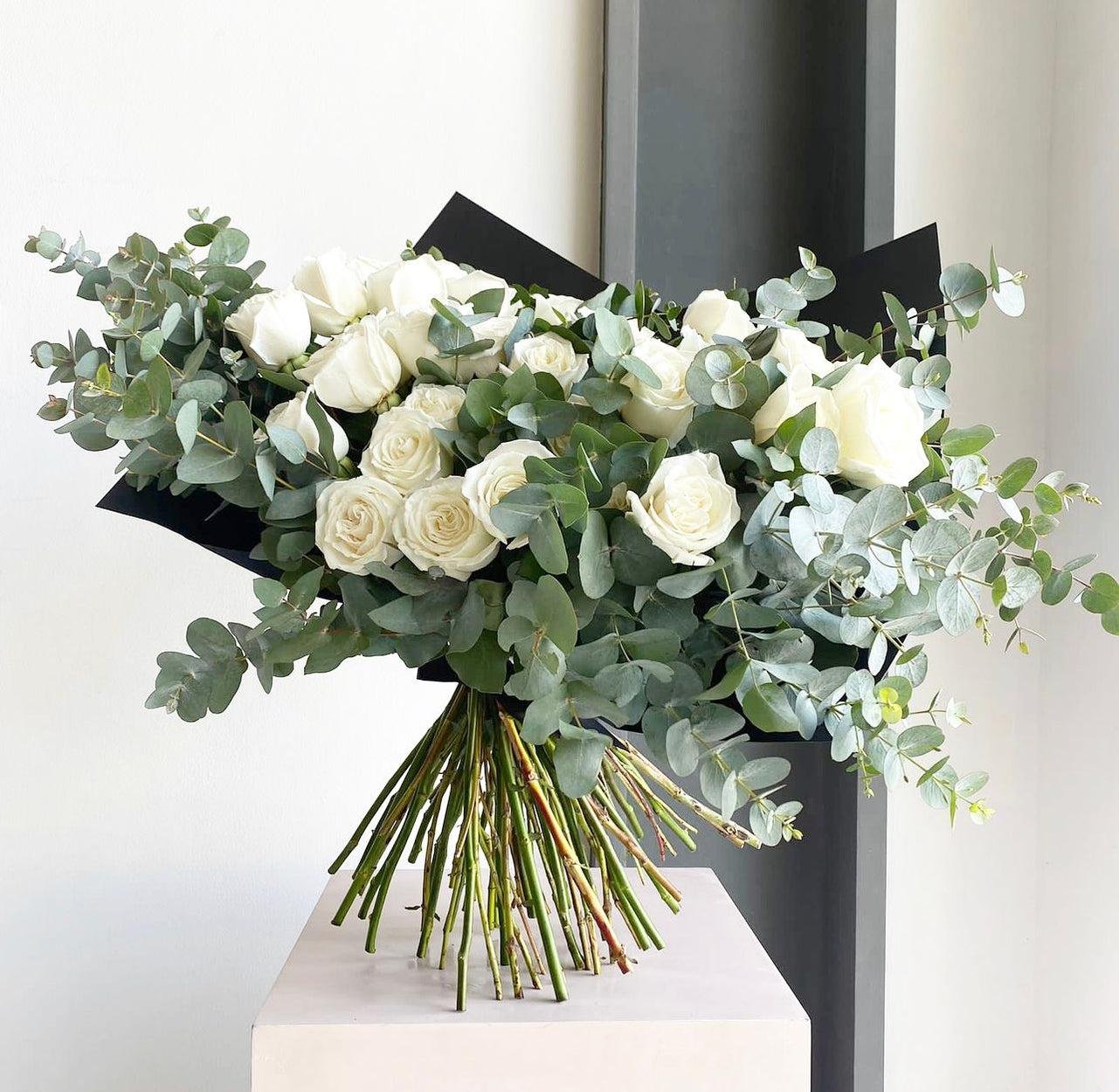 Elegant white flower bouquet featuring fresh white roses and eucalyptus greenery wrapped in black floral paper, perfect for weddings, anniversaries, luxury gifts, and modern home décor.