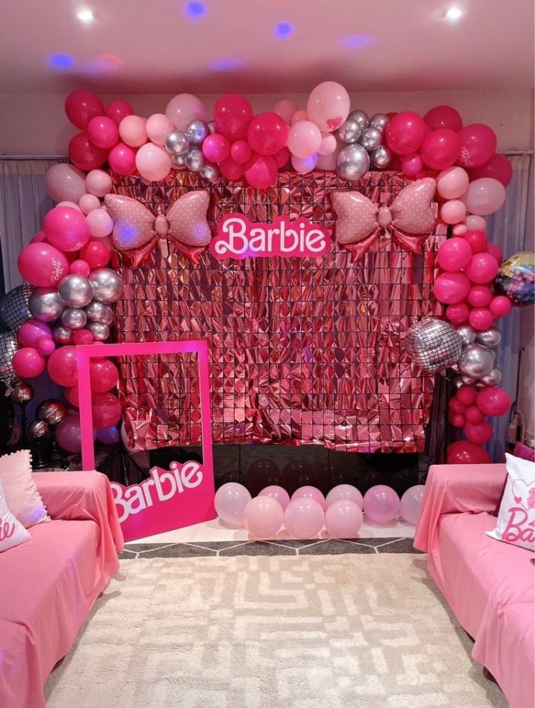 Barbie birthday party backdrop with pink, hot pink, and silver balloons, large decorative bows, a Barbie sign, and a stylish pink photo booth setup.